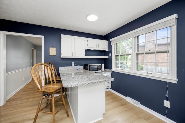 2912 Jason Ct, Lexington, KY 40503 - kitchen featuring stainless steel microwave, light wood-style flooring, white cabinets, and a kitchen bar