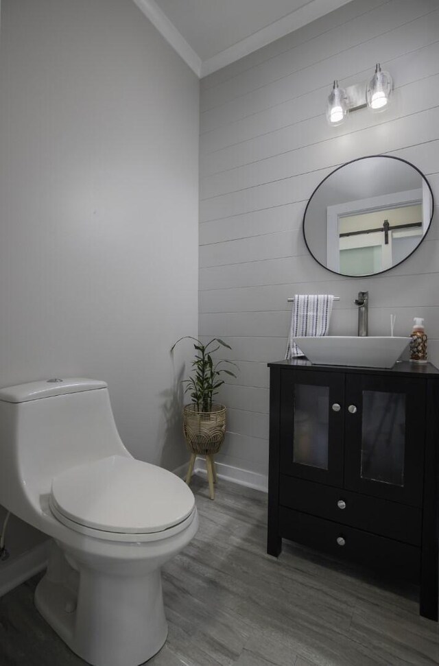 half bathroom featuring toilet, ornamental molding, wood finished floors, vanity, and wooden walls