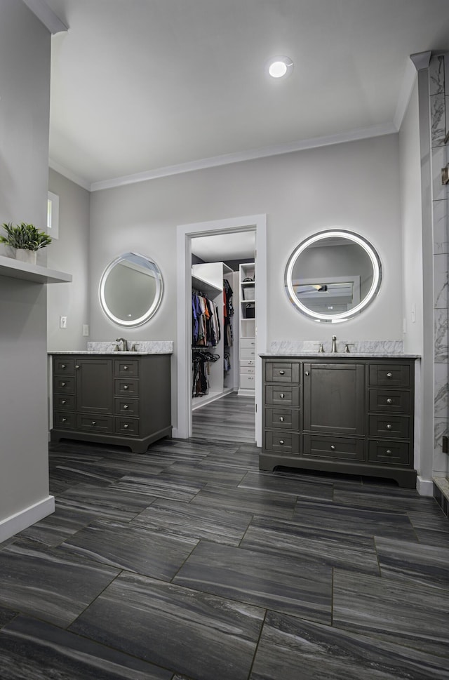 full bathroom with ornamental molding, two vanities, a walk in closet, and baseboards