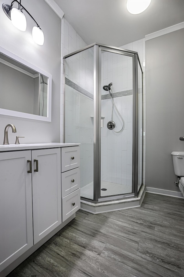 bathroom with a stall shower, vanity, wood finished floors, toilet, and baseboards