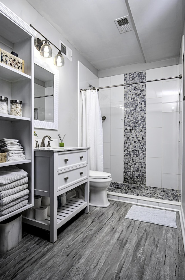 bathroom featuring wood finished floors, a tile shower, toilet, and vanity