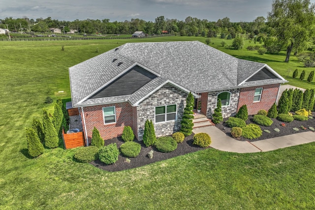 view of front facade featuring roof with shingles, a front yard, brick siding, and stone siding