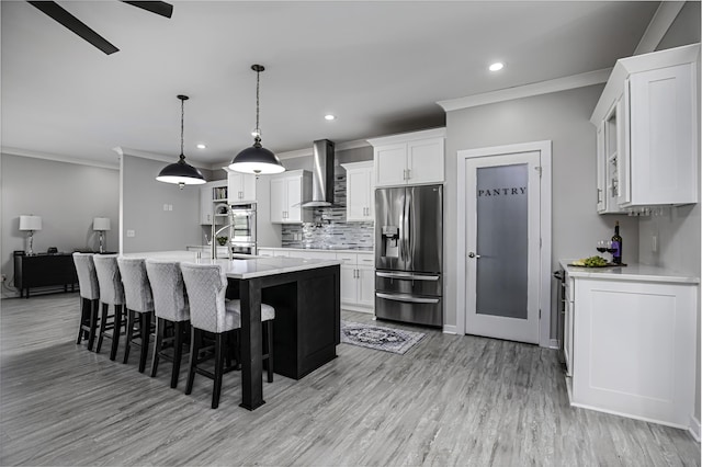 kitchen with appliances with stainless steel finishes, wall chimney range hood, crown molding, light wood-style flooring, and recessed lighting