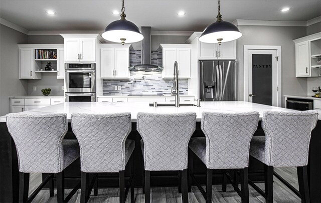 kitchen with wall chimney exhaust hood, open shelves, stainless steel appliances, a large island with sink, and backsplash