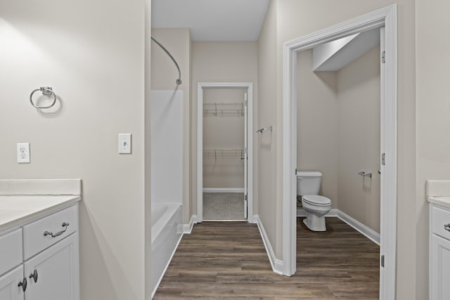 bathroom featuring vanity, toilet, wood finished floors, baseboards, and a walk in closet
