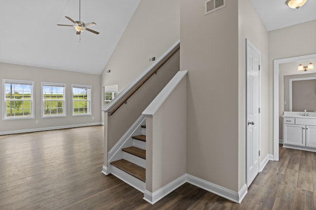stairway with wood finished floors, ceiling fan, baseboards, and high vaulted ceiling