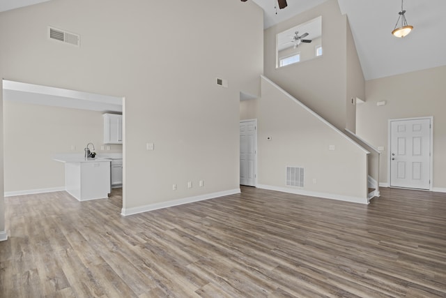 unfurnished living room featuring high vaulted ceiling, a ceiling fan, stairs, wood finished floors, and baseboards