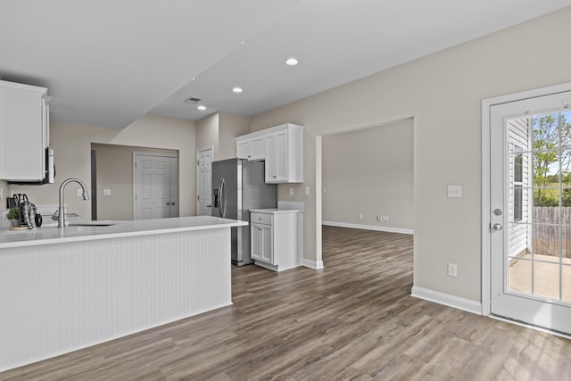kitchen with a sink, stainless steel refrigerator with ice dispenser, dark wood finished floors, white cabinets, and light countertops