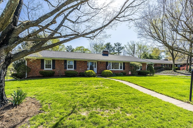 single story home featuring brick siding, a chimney, and a front yard