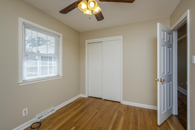 unfurnished bedroom featuring wood finished floors, baseboards, a closet, and a ceiling fan