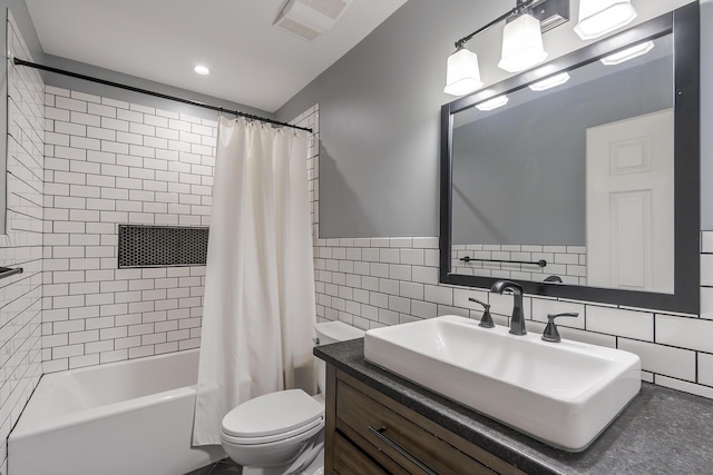full bath featuring tile walls, toilet, vanity, shower / bath combo with shower curtain, and wainscoting