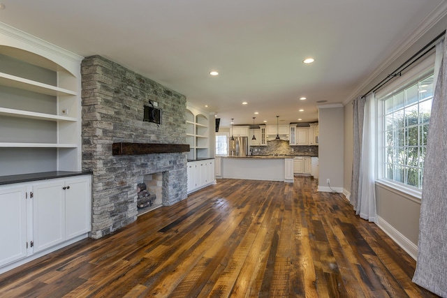 unfurnished living room featuring dark wood finished floors, a stone fireplace, crown molding, recessed lighting, and built in shelves