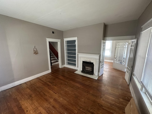 unfurnished living room featuring dark wood-style floors, baseboards, a tile fireplace, and stairs