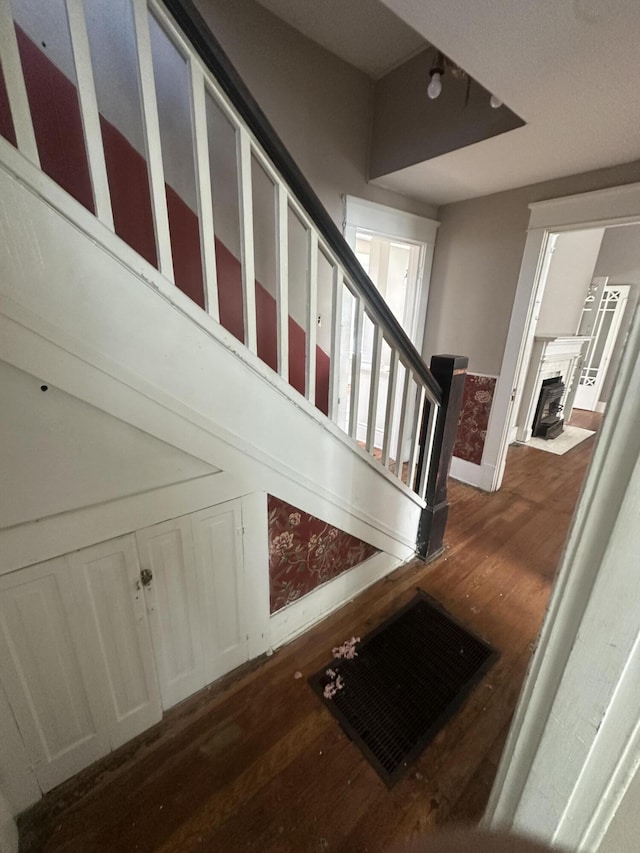 stairs featuring wood finished floors, baseboards, and a fireplace with flush hearth