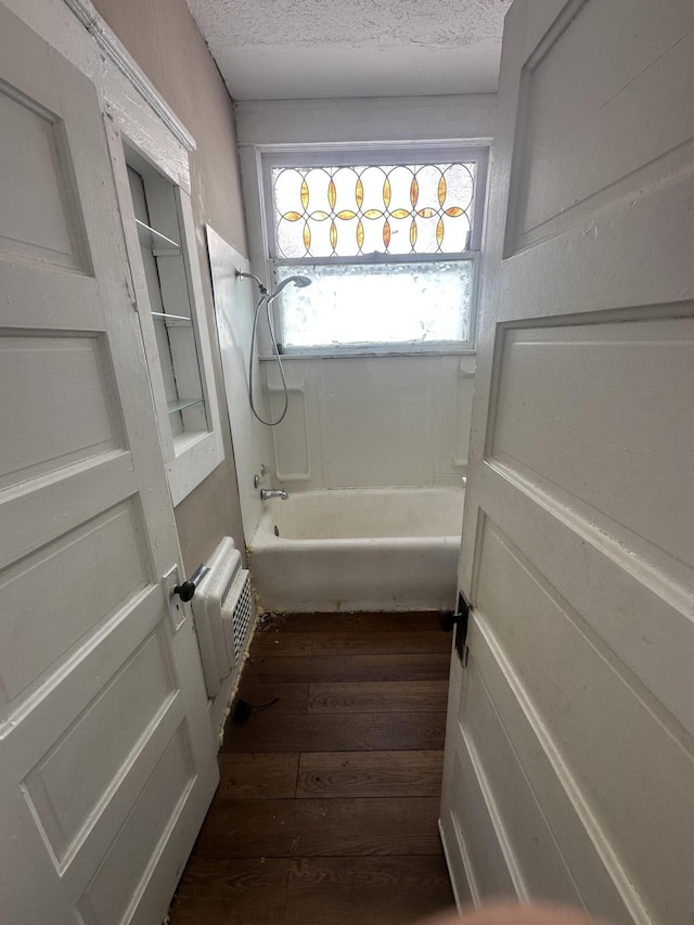 bathroom with hardwood / wood-style floors, tub / shower combination, a textured ceiling, and an AC wall unit