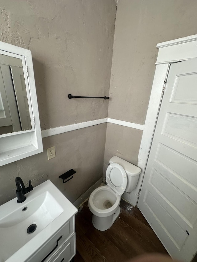 half bathroom with wood finished floors, toilet, and vanity