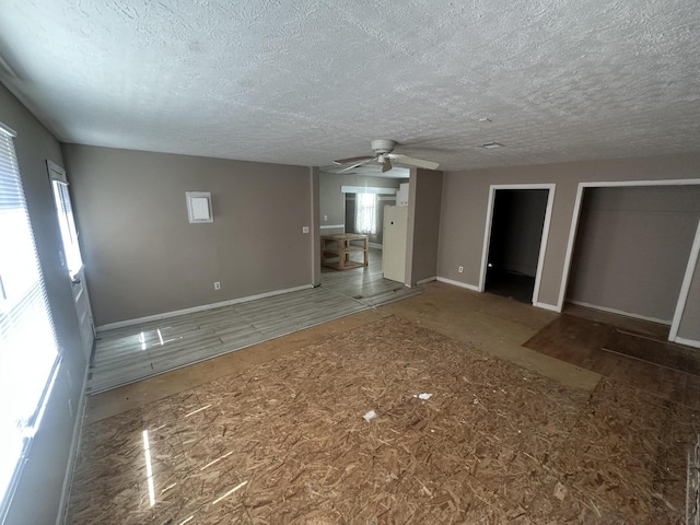 unfurnished living room featuring a textured ceiling, a ceiling fan, and baseboards