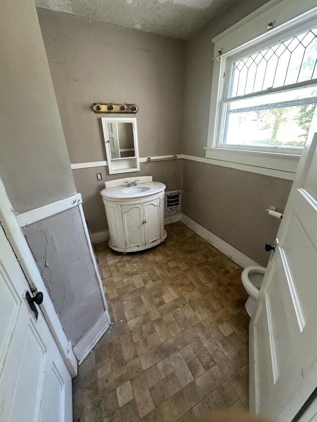 half bath with vanity, baseboards, brick patterned flooring, and toilet
