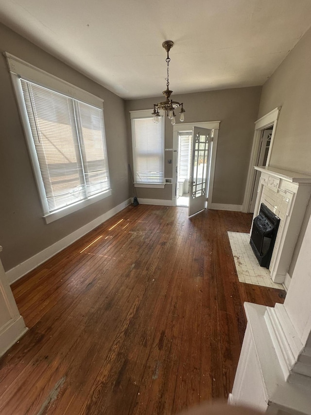 unfurnished dining area featuring a chandelier, dark wood-style floors, a fireplace with flush hearth, and baseboards