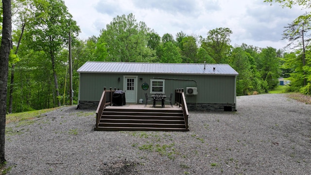 back of property featuring metal roof, a wooden deck, a forest view, and crawl space