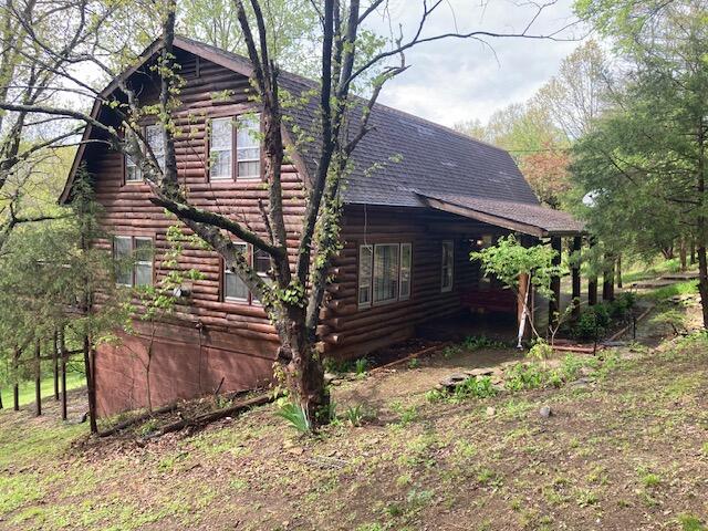 view of side of home with a shingled roof and log exterior