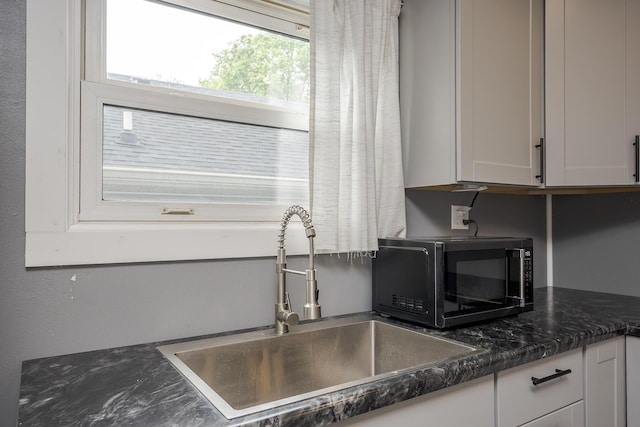 kitchen featuring a sink, black microwave, and white cabinetry