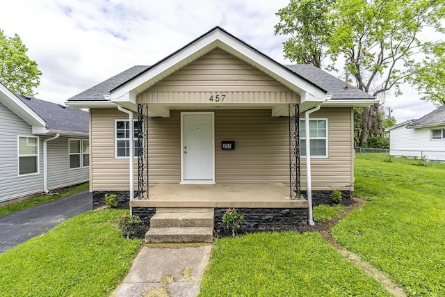 bungalow-style home with a porch, roof with shingles, a front lawn, and fence