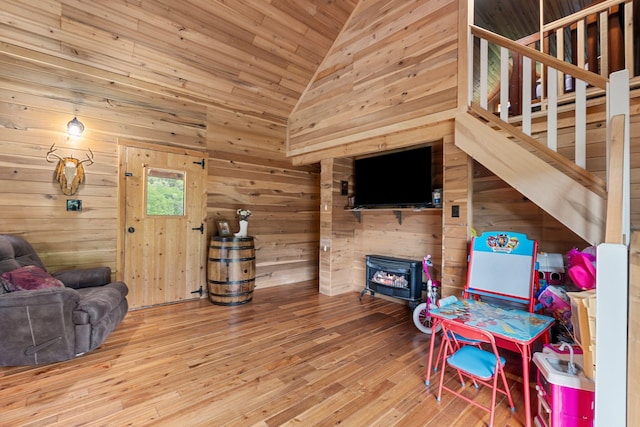 interior space with a wood stove, wood walls, wood-type flooring, and high vaulted ceiling