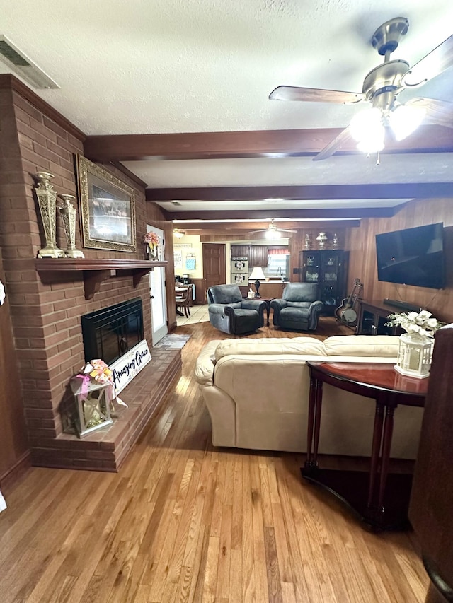 living area featuring light wood-type flooring, a brick fireplace, ceiling fan, and a textured ceiling