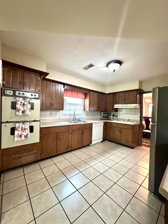 kitchen featuring light tile patterned floors, white appliances, a sink, light countertops, and tasteful backsplash