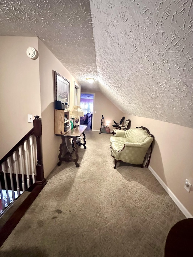 sitting room with carpet flooring, an upstairs landing, a textured ceiling, baseboards, and lofted ceiling