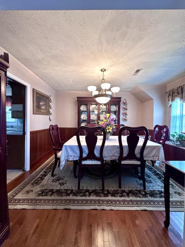 dining area featuring wood finished floors, a wainscoted wall, a notable chandelier, a textured ceiling, and visible vents