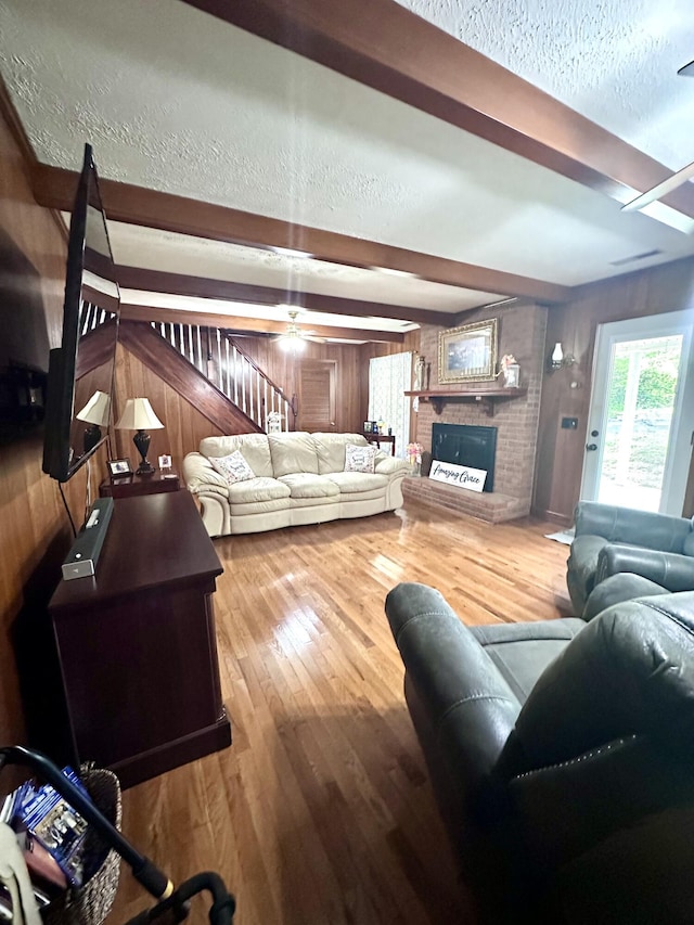living area featuring beam ceiling, wooden walls, a fireplace, and wood finished floors