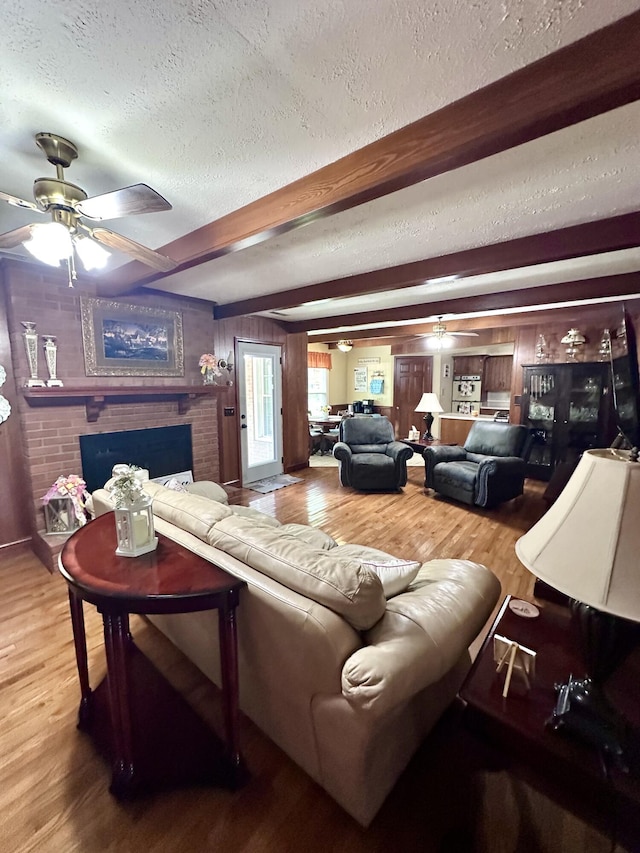living area featuring light wood finished floors, a ceiling fan, beam ceiling, a fireplace, and a textured ceiling