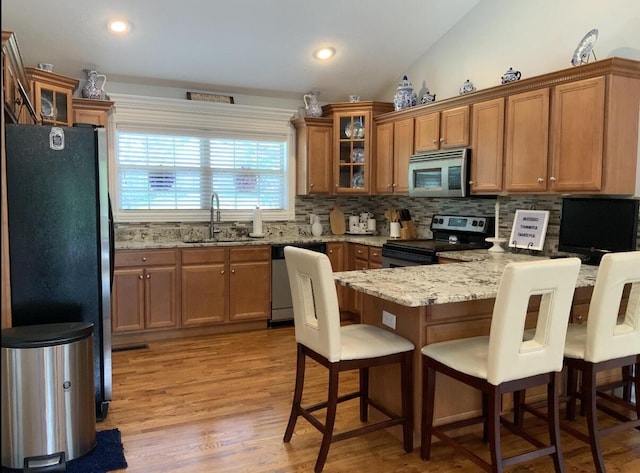 kitchen featuring a sink, a peninsula, stainless steel appliances, brown cabinets, and glass insert cabinets