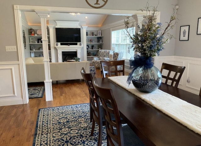 dining space featuring wood finished floors, a fireplace, wainscoting, vaulted ceiling, and built in shelves