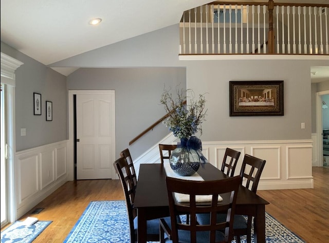 dining space with light wood finished floors, lofted ceiling, a decorative wall, and a wainscoted wall