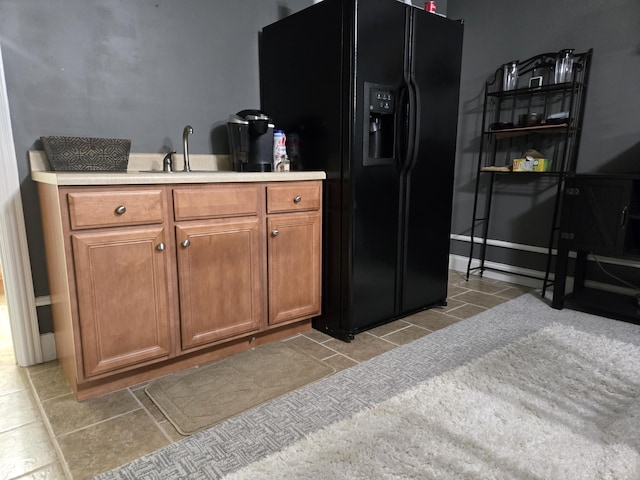 kitchen with light tile patterned floors, black fridge with ice dispenser, a sink, brown cabinets, and light countertops