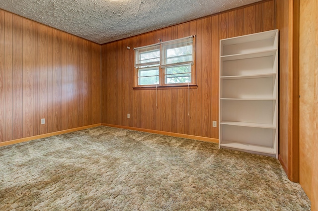 carpeted empty room featuring a textured ceiling, wood walls, and baseboards