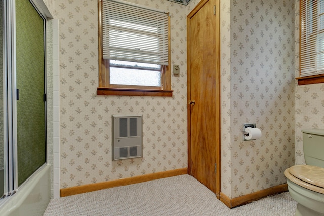 bathroom featuring heating unit, toilet, and bath / shower combo with glass door