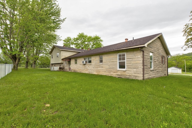 back of property with stone siding, an outbuilding, fence, and a lawn