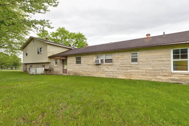 rear view of house with stone siding, a shingled roof, a lawn, and a wall unit AC