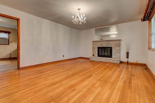 unfurnished living room with light wood finished floors, an inviting chandelier, cooling unit, baseboards, and a stone fireplace