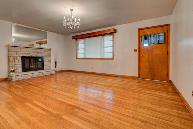 unfurnished living room with baseboards, a stone fireplace, a notable chandelier, and wood finished floors