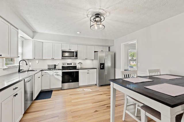 kitchen with appliances with stainless steel finishes, a sink, light wood finished floors, white cabinetry, and a textured ceiling