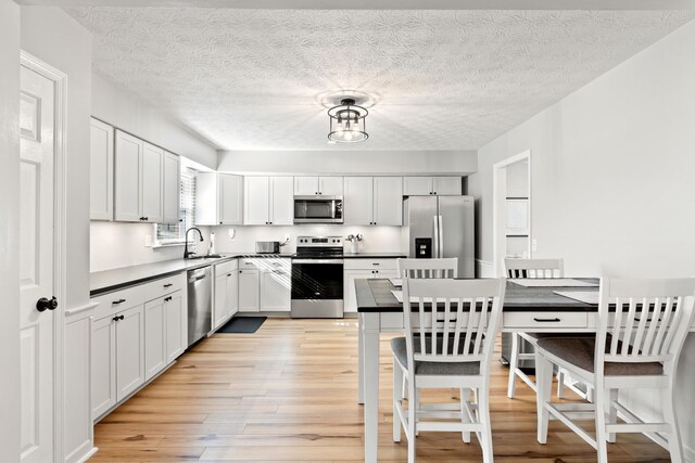 kitchen featuring stainless steel appliances, light wood finished floors, dark countertops, and a textured ceiling