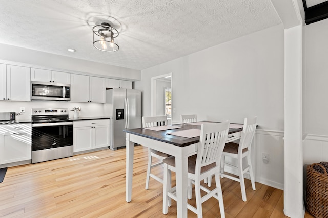 kitchen featuring stainless steel appliances, light wood-type flooring, dark countertops, white cabinetry, and a textured ceiling