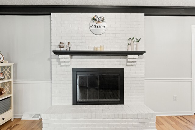 detailed view of wood finished floors, a wainscoted wall, and a fireplace