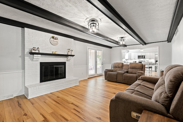 living area with beamed ceiling, light wood finished floors, a wainscoted wall, and a fireplace