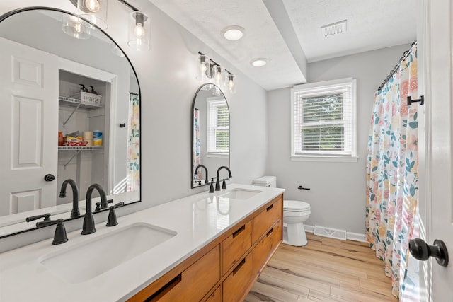 bathroom with toilet, wood finished floors, double vanity, and baseboards